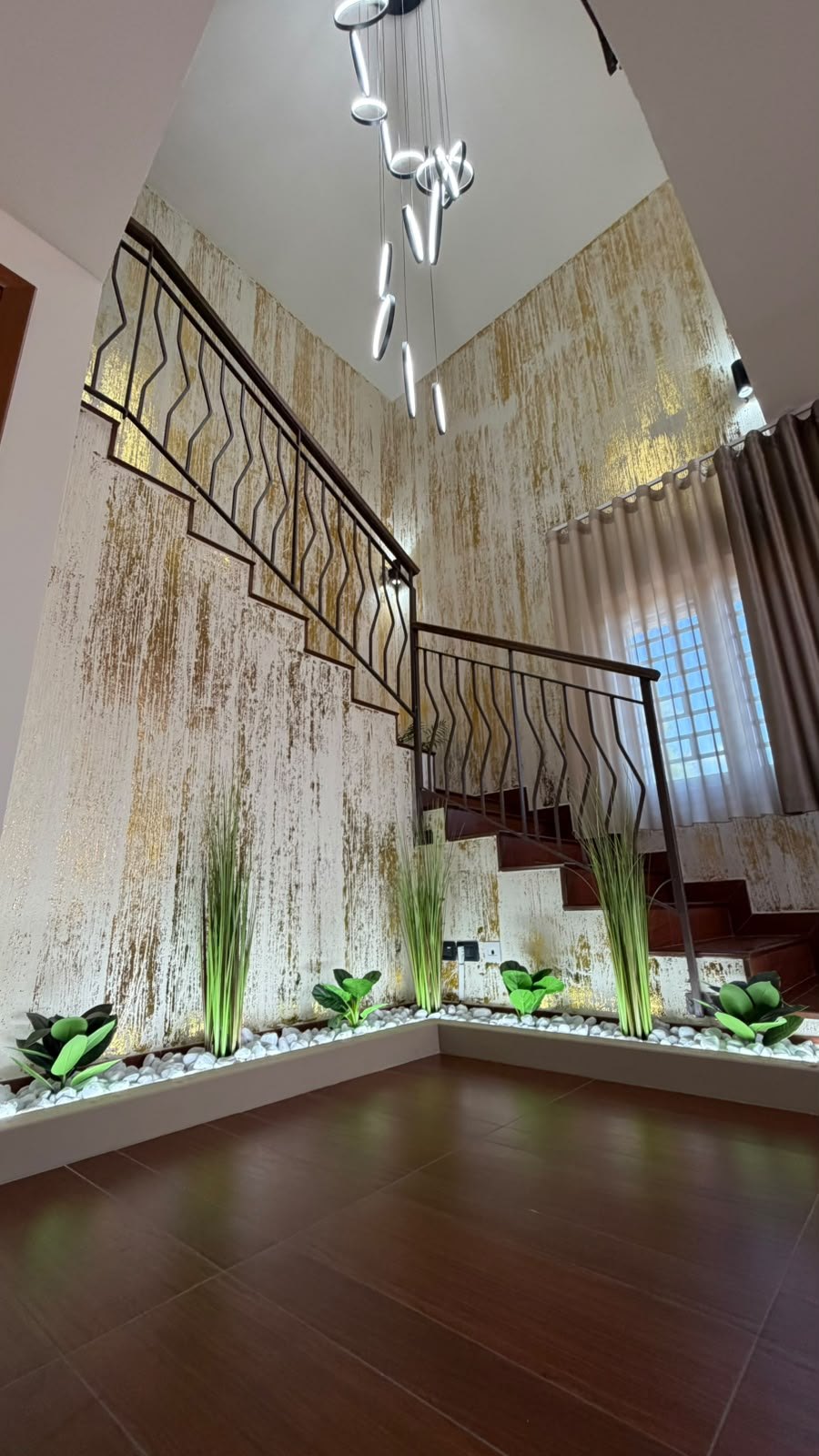 Scala con ringhiera scura, pareti bianche e oro, lampadario LED e aiuola di ciottoli a Villa Vittoria Relais