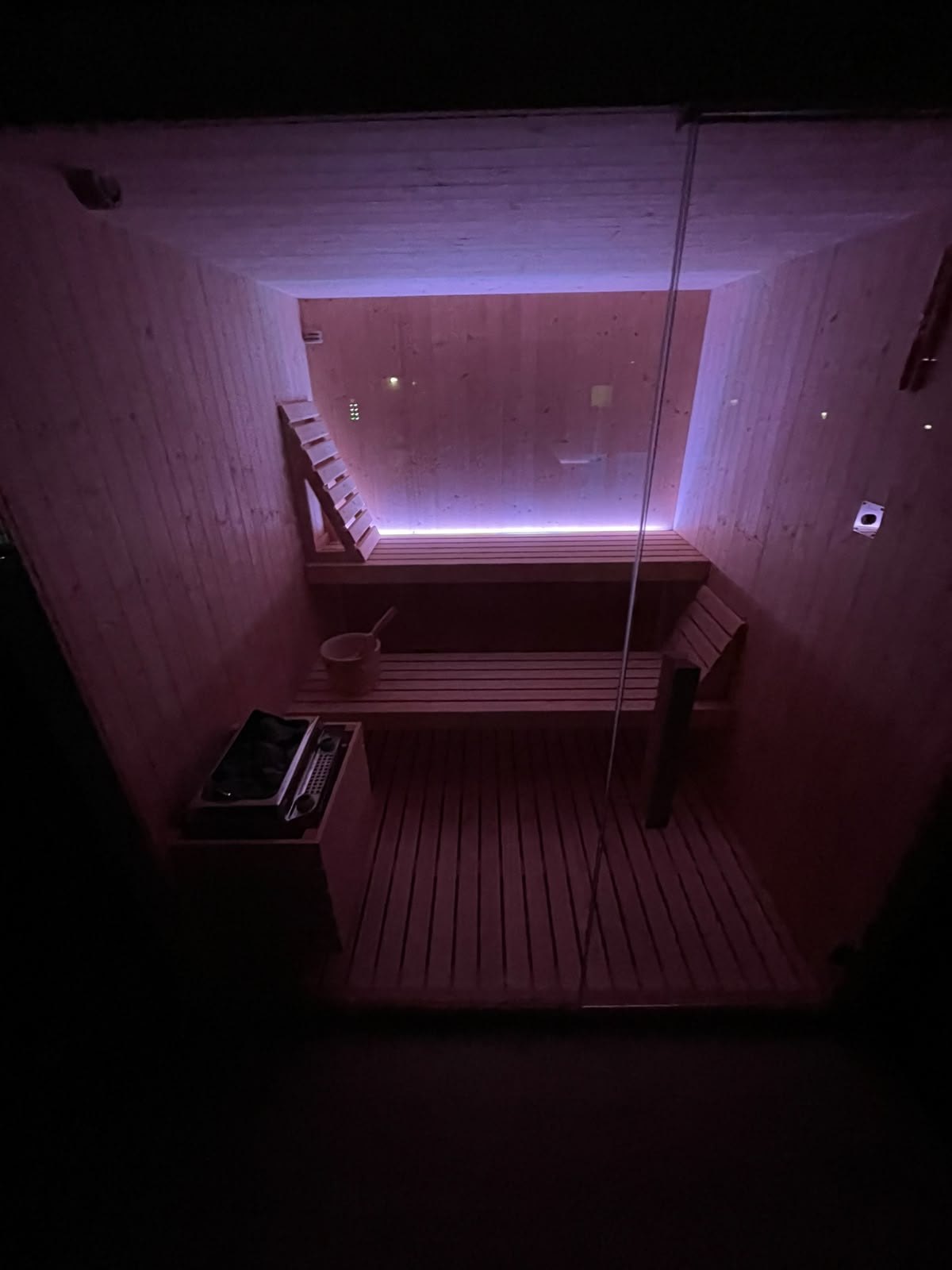 Sauna finlandese di Villa Vittoria Relais in legno chiaro con panche a gradoni, stufa e secchio, illuminata da luci viola